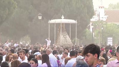 Multitud en evento multitudinario, ambiente polvoriento, personas vestidas de blanco alrededor de una estructura. Posiblemente Romera del Roco.